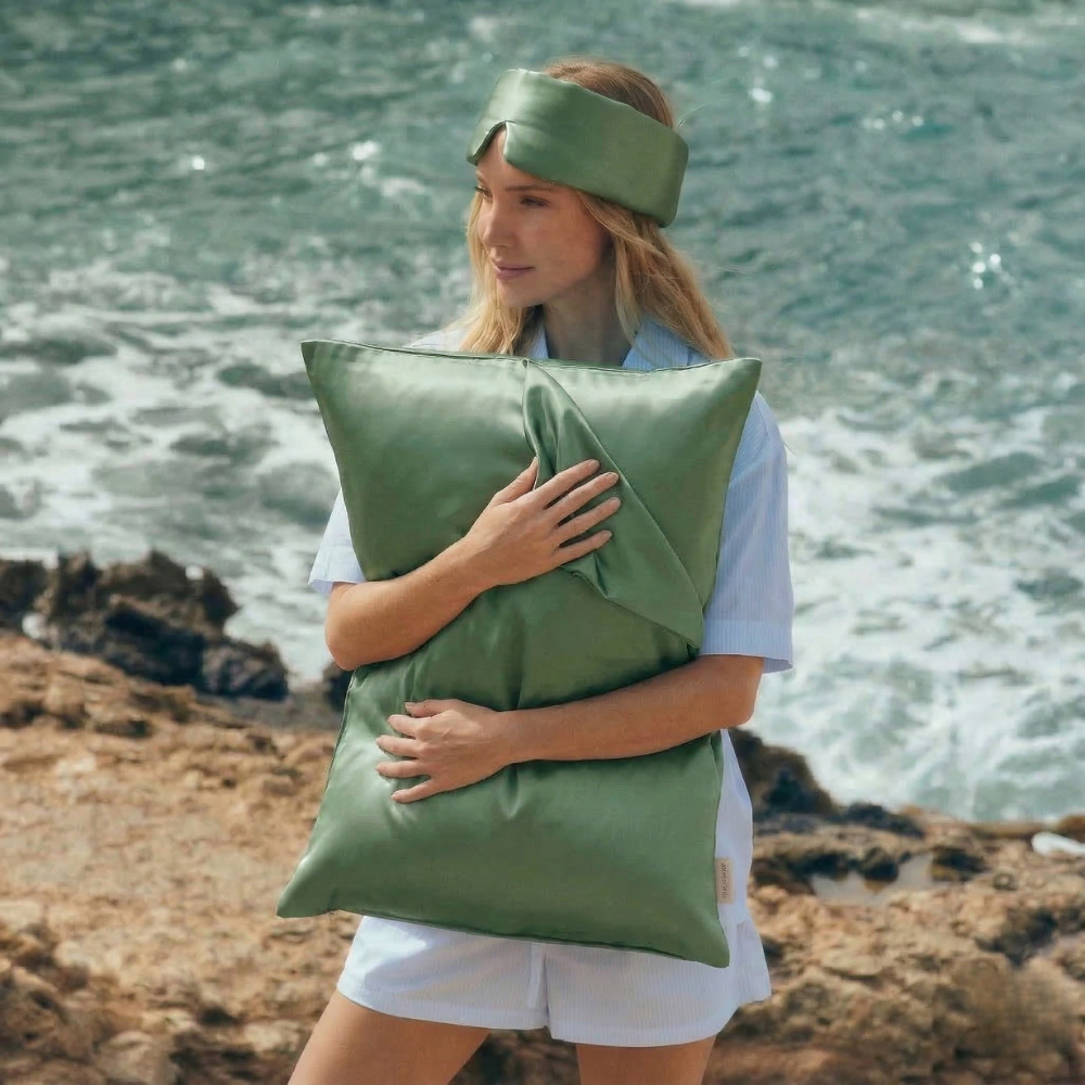 Woman holding GLOWE silk pillowcase in Olive Mist outdoors, lifestyle shot